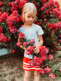 Low angle view of girl standing against red flowering plants