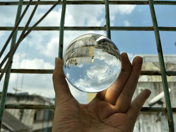 Close-up of hand holding glass ball against window