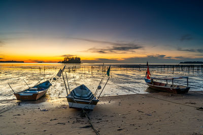 Boat moored on beach against sky during sunset