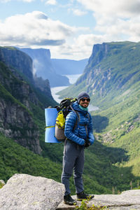 Full length of male hiker standing against mountains on rocks at gros morne national park