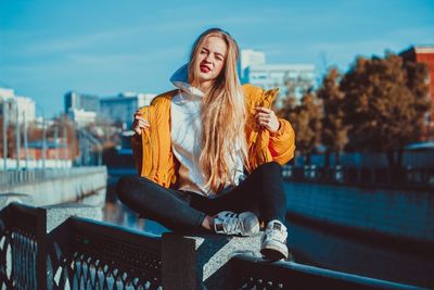 Young woman sitting on railing against blurred background