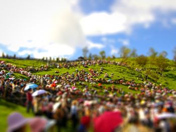 Tilt-shift image of crowd on field against sky