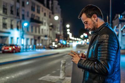 Side view of young man using smart phone on city street