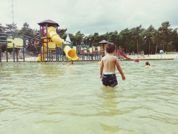 Rear view of shirtless boy in swimming pool against sky