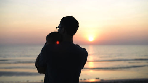 Silhouette couple standing at beach during sunset