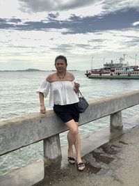 Full length portrait of woman standing by railing against sea and sky