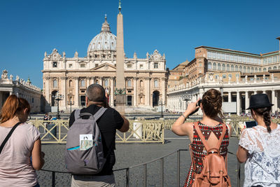 Rear view of people photographing st peters basilica in city