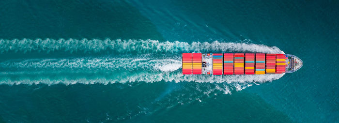 Aerial top view of cargo ship with contrail in the ocean sea ship carrying container 