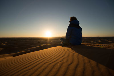 Man sitting on sand at beach against clear sky