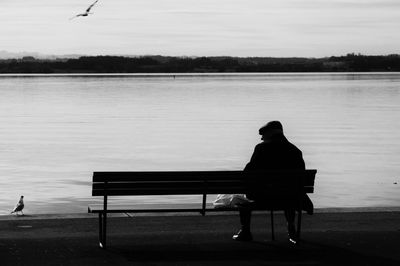Rear view of man sitting by lake on bench