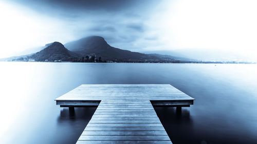 Jetty on pier by lake against sky