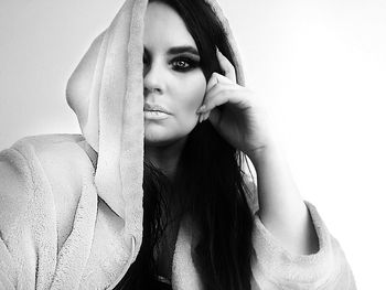 Portrait of young woman in hooded jacket against white background