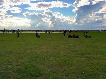 People on grassy field against cloudy sky