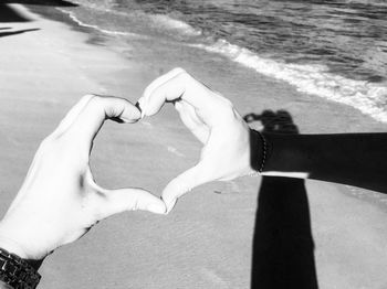 Cropped hands of couple making heart shape with hands on shore at beach