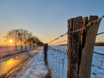 Wooden fence on snow against sky during sunset