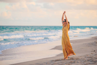 Rear view of woman standing at beach against sky