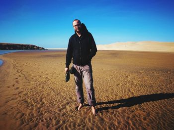 Full length of man standing on sand at beach against clear sky