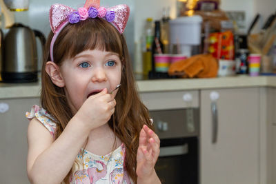 Portrait of cute girl at home eating with a spoon