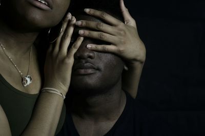 Woman covering eyes of man against black background