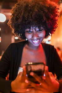 Smiling young woman using mobile phone in bar