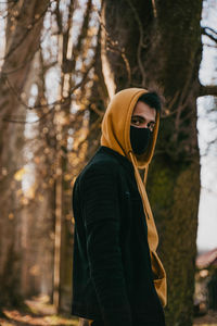 Portrait of young man wearing mask standing by tree