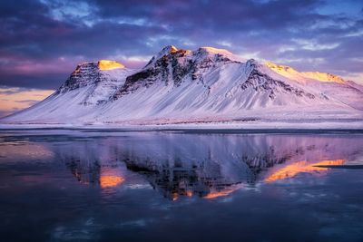 Scenic view of lake by snowcapped mountains against sky during sunset