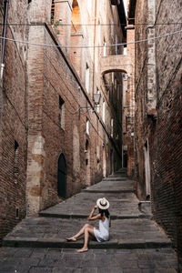 Full length of woman sitting on footpath amidst buildings in city