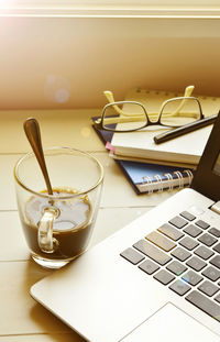 Laptop with black coffee and spectacles on spiral diary kept on wooden table