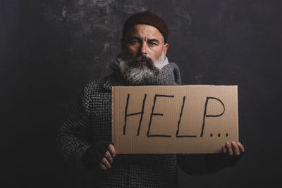 Sad exhausted homeless man in red cap and street clothes holding a cardboard sign with the word help