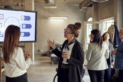 Businesswomen discussing by television near colleagues in office