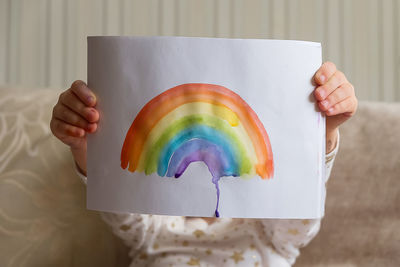 Kid painting rainbow at home. girl holding adrawing with rainbow. stay at home 