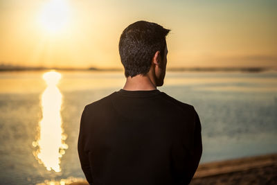 Rear view of man standing at beach during sunset