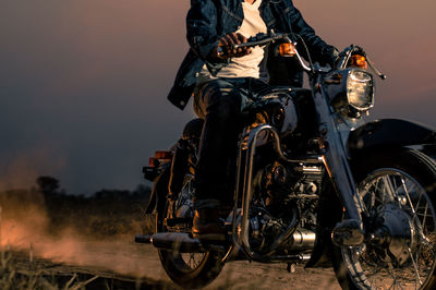 Low section of man riding bicycle on road against sky during sunset