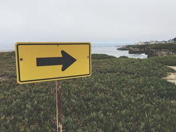 Directional sign at beach against sky