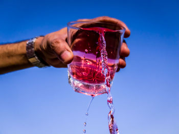 Close-up of hand holding drink against blue sky