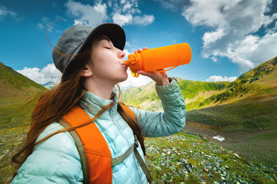 Young sports girl stands against the backdrop of a stunning mountain view and drinks clean water