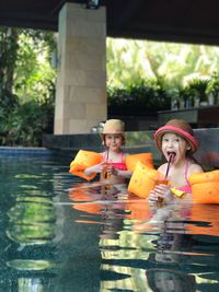 Portrait of sisters having drink while swimming in pool