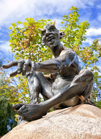 Low angle view of statue by tree against sky