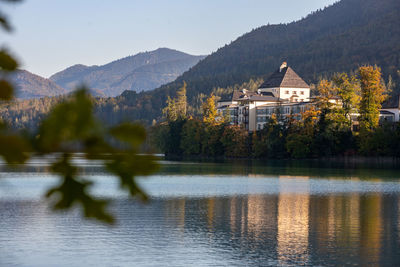 Lake by buildings and mountains against sky