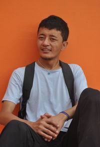 An asian guy looking sideways, sitting against orange wall background with copy space 