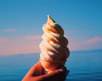 Cropped hand holding ice cream against sea