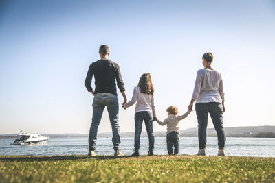 Rear view of family standing by lake against sky