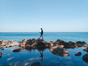 Rear view of man walking at beach against clear sky