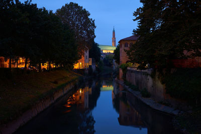 Illuminated buildings by lake against sky