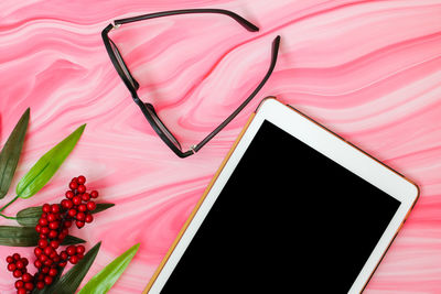 Directly above shot of digital tablet with berries and eyeglasses on pink table