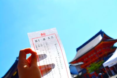 Cropped hand of woman holding pamphlet against clear blue sky