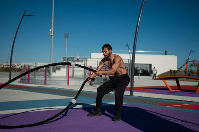 Muscular man doing battle rope outdoors