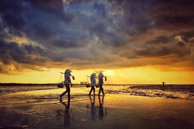 Rear view of three people walking on beach