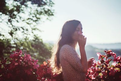 Side view of woman standing by flowering plants against sky