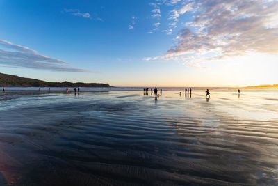 People on beach against sky during sunset